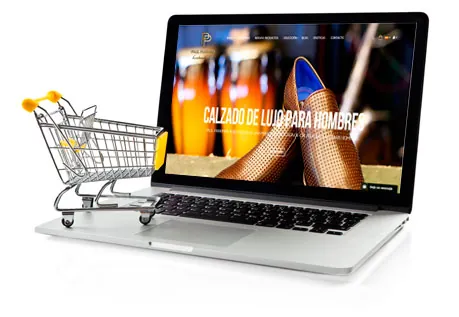 Portátil con una tienda online de calzado de lujo para hombres, junto a un carrito de compras